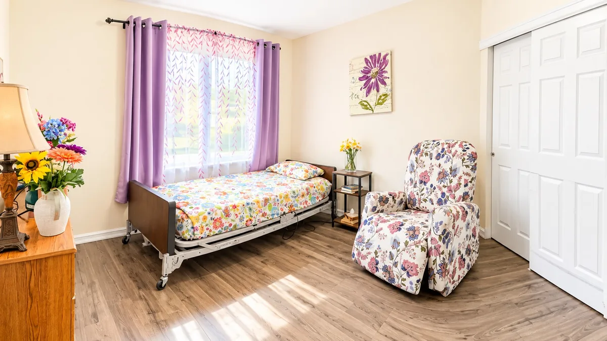 A resident bedroom with a window, an armchair and fresh flowers